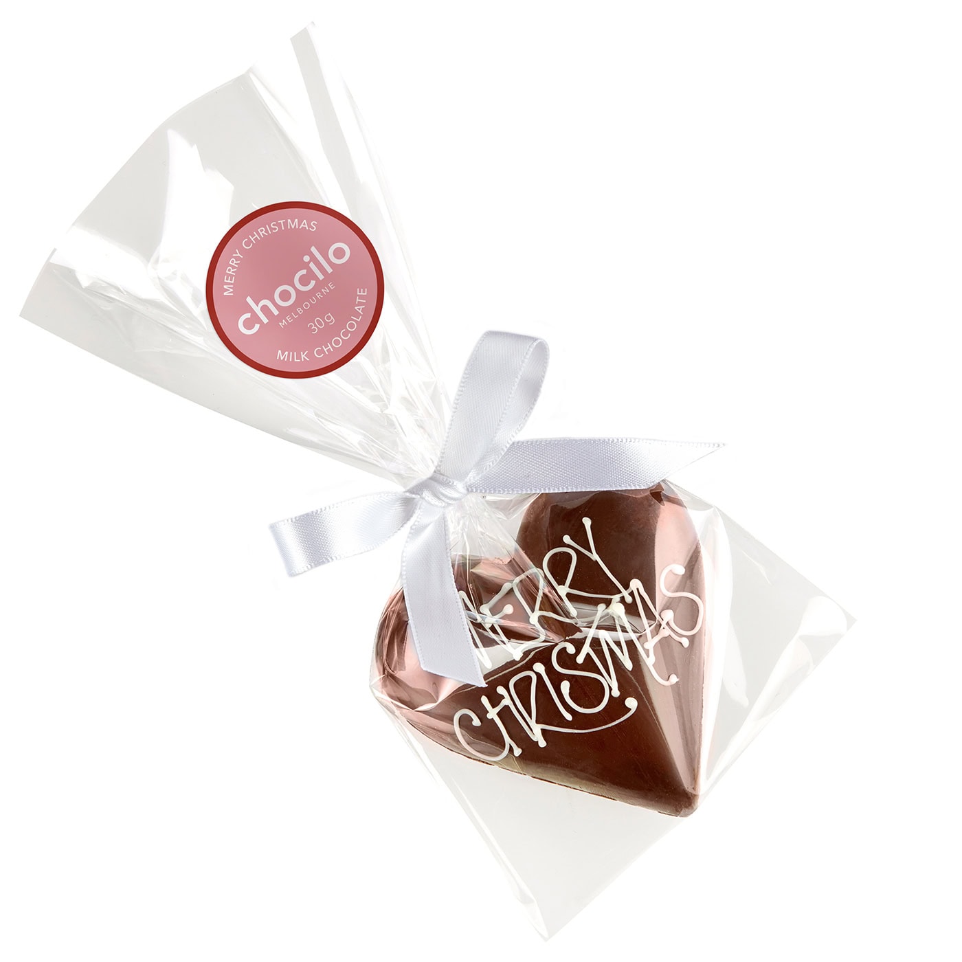A heart-shaped milk chocolate filled with smooth hazelnut praline, decorated with white icing that reads 'MERRY CHRISTMAS', individually wrapped in clear cellophane with a white ribbon.