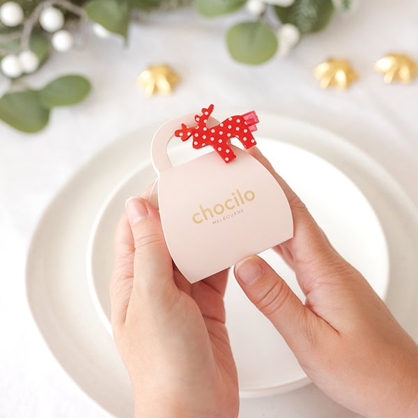 Chocilo Melbourne 2 Pack Christmas Milk Chocolate Caramels with a sugar decoration in a light pink cardboard handbag and a festive red and white reindeer clip.